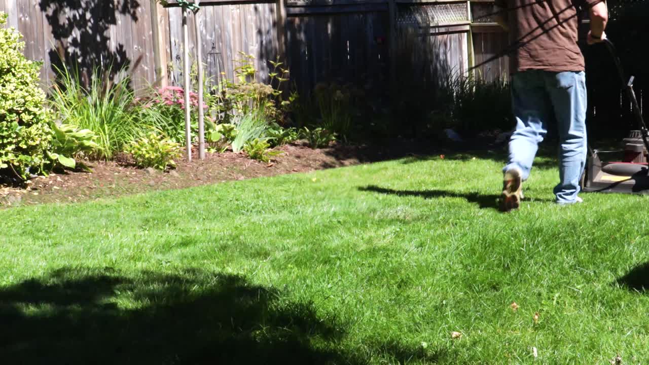 un hombre hace dos pases con una cortadora de césped con un jardín al fondo