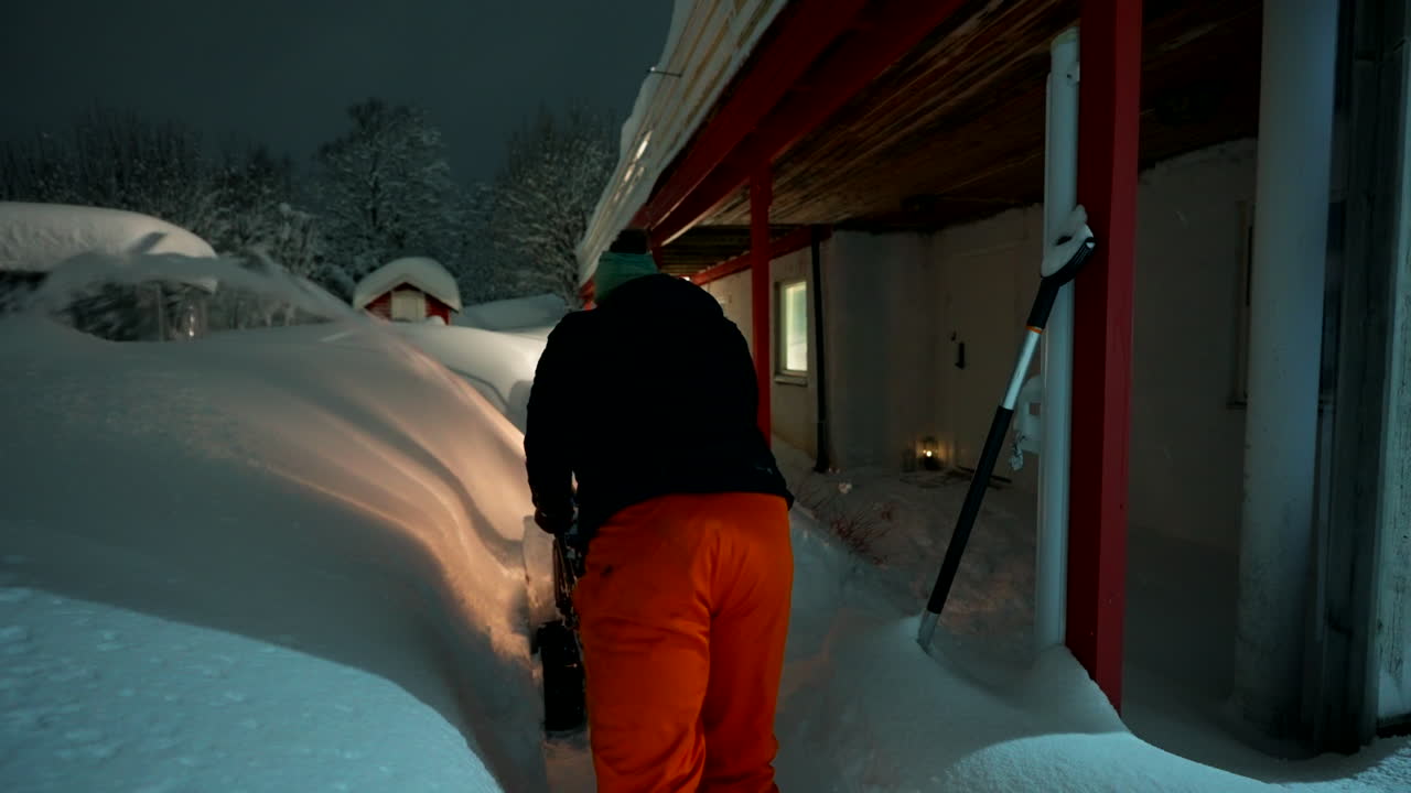 A snowplow working near buildings at night, snowy urban winter atmosphere in Norway with snow flying up out of path