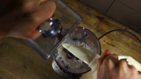 slow motion top down of female person pouring milk and fresh berries for milkshake in blender. close up shot.