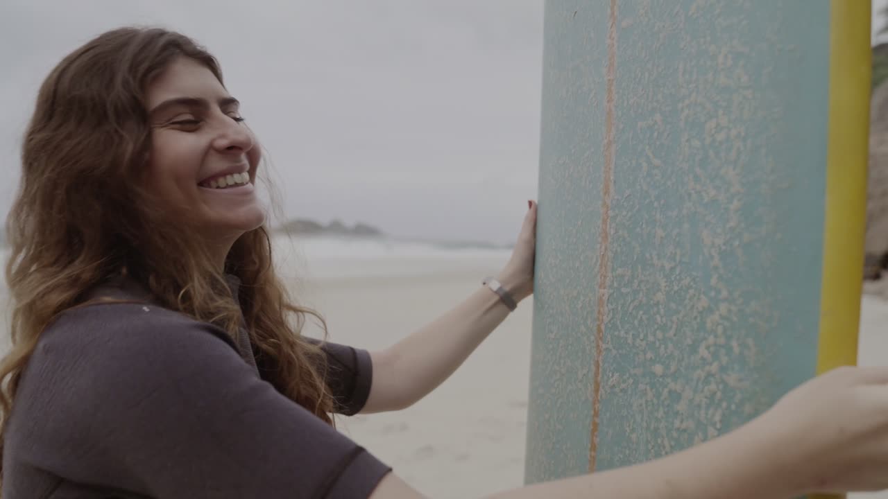 Smiling woman waxing a surfboard on the beach