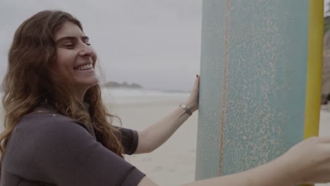 smiling woman waxing a surfboard on the beach