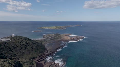 aerial dolly along jagged volcanic cliffs with sheets of slick rock along coast to low island in port kembla nsw australia