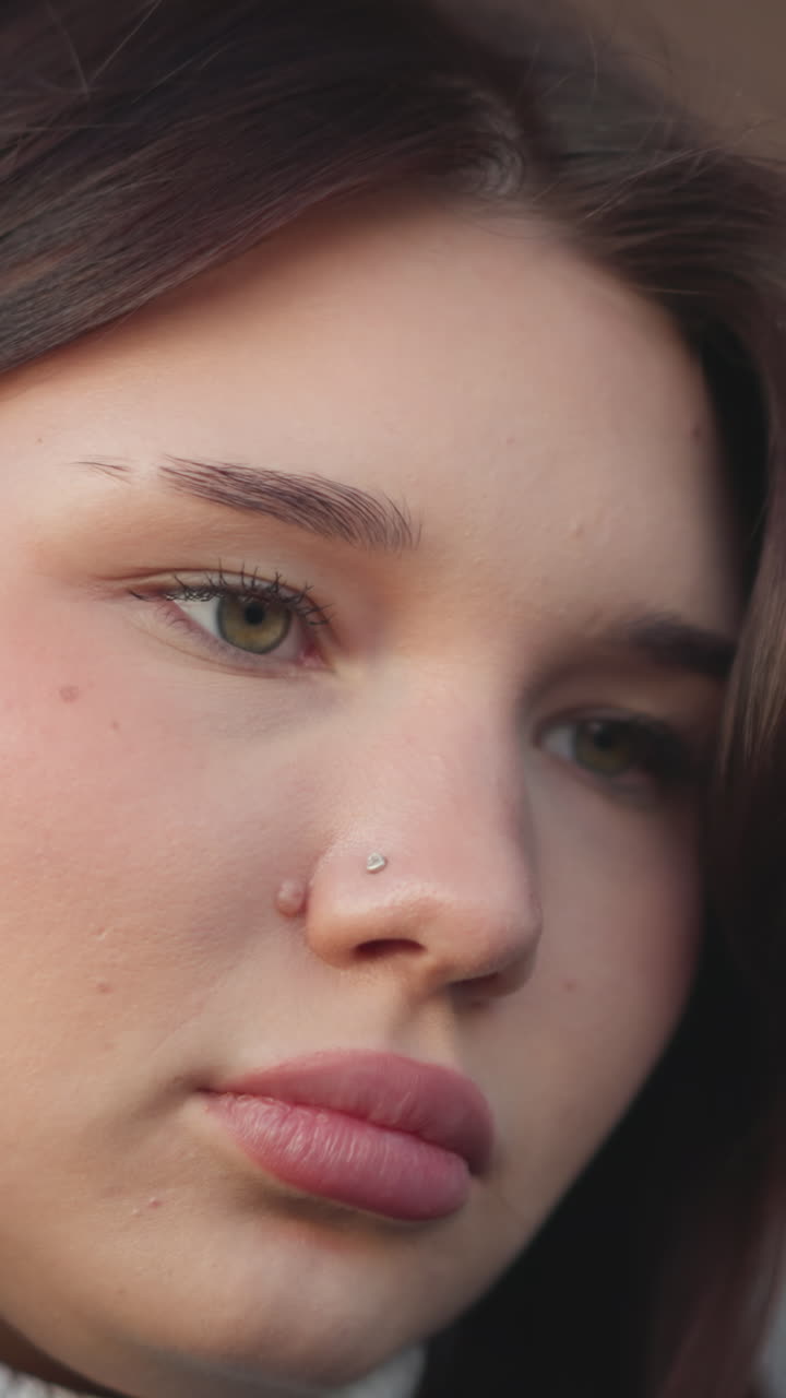 primer plano de una mujer con labios rosados que se centra en algo delante de ella, mostrando su belleza natural, con un anillo sutil en la nariz y una expresión suave y enfocada en un fondo borroso