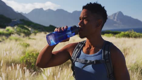 hombre afroamericano haciendo ejercicio al aire libre bebiendo agua en el campo en una costa