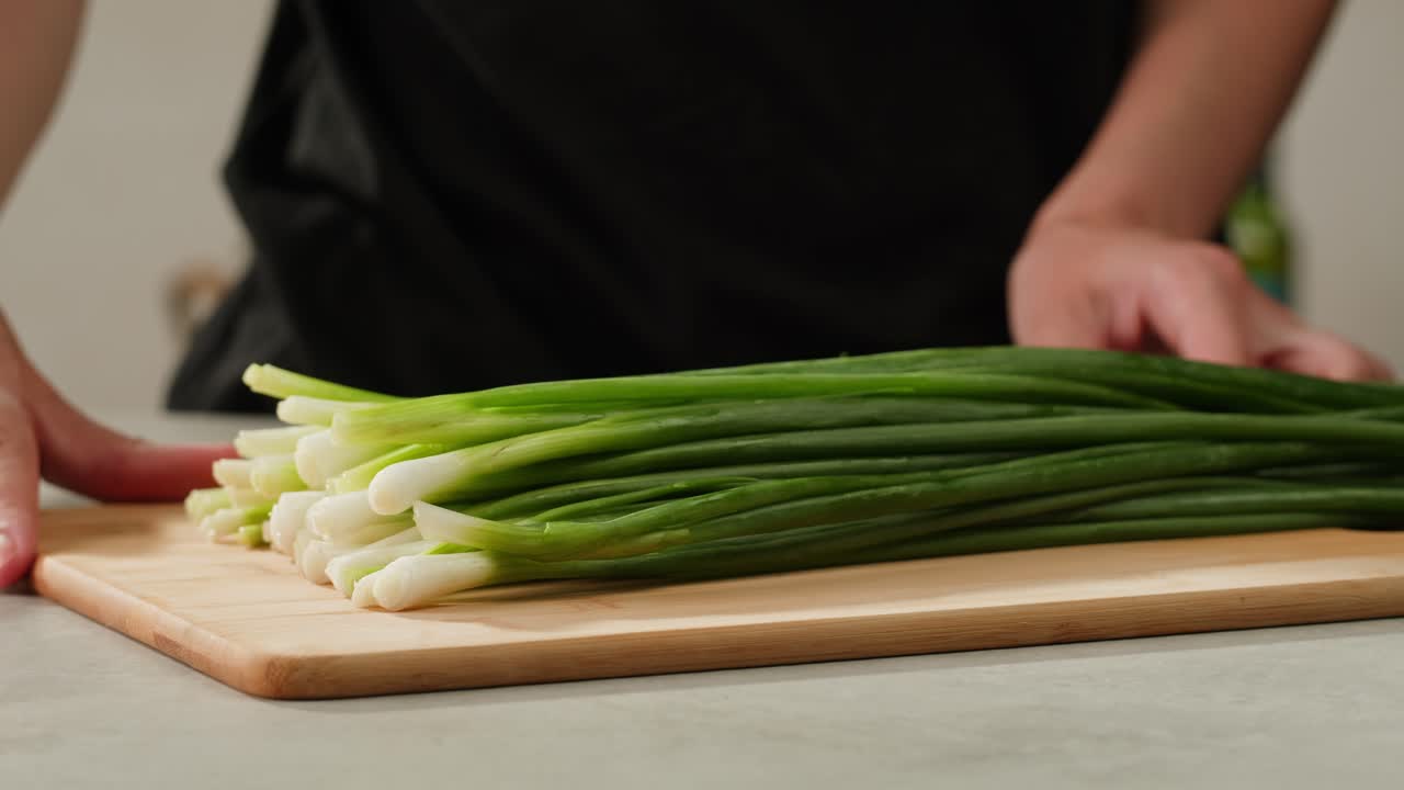 Cutting fresh green onions on a cutting board, close up chef cooking green vegan salad.