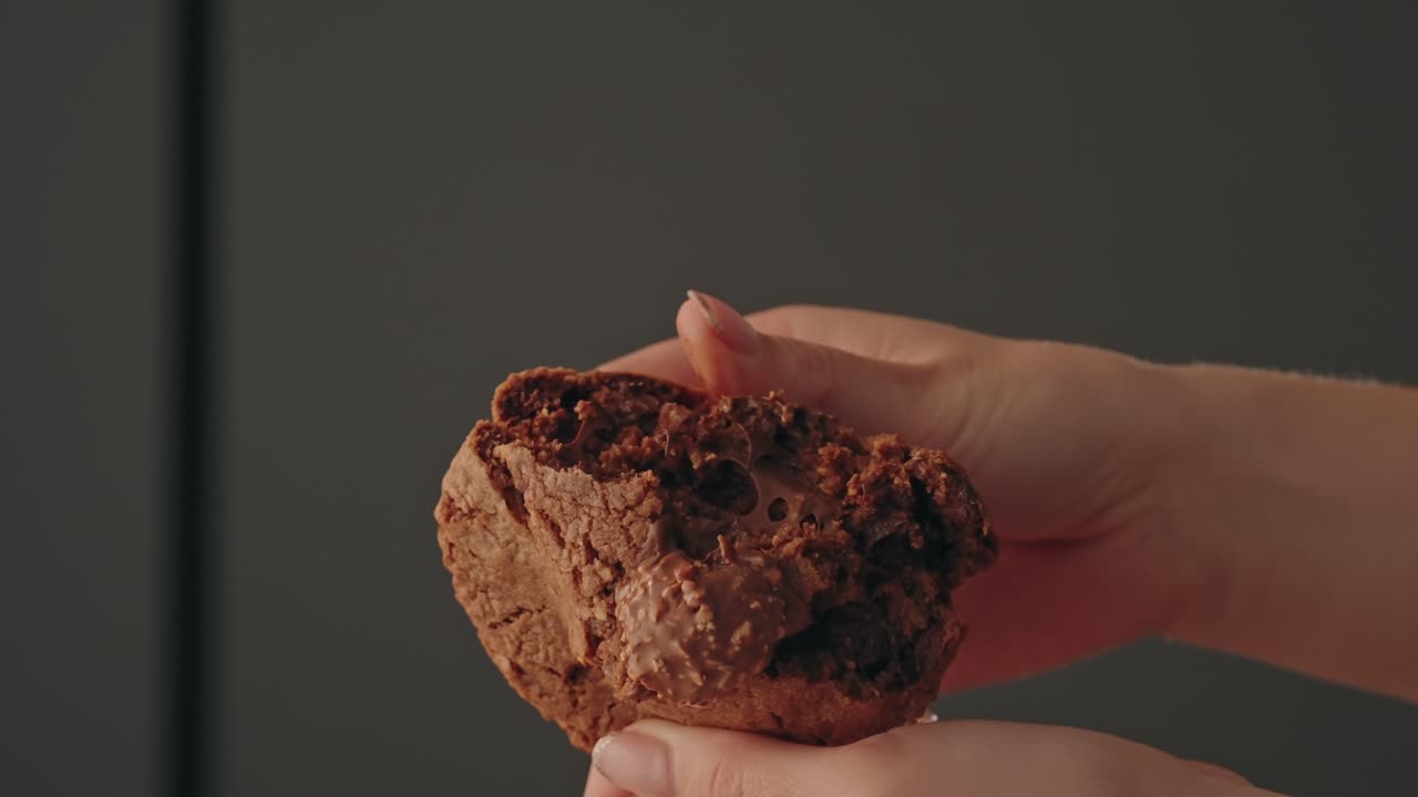 Close up of hands splitting chocolate cookie showing soft melted interior