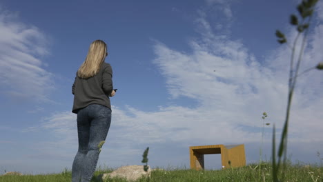 young woman with remote controller and quadcopter drone under beautiful sky on sunny summer day, back view, slow motion