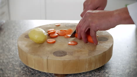 a chef is chopping carrots in a kitchen on a chopping board with a knife