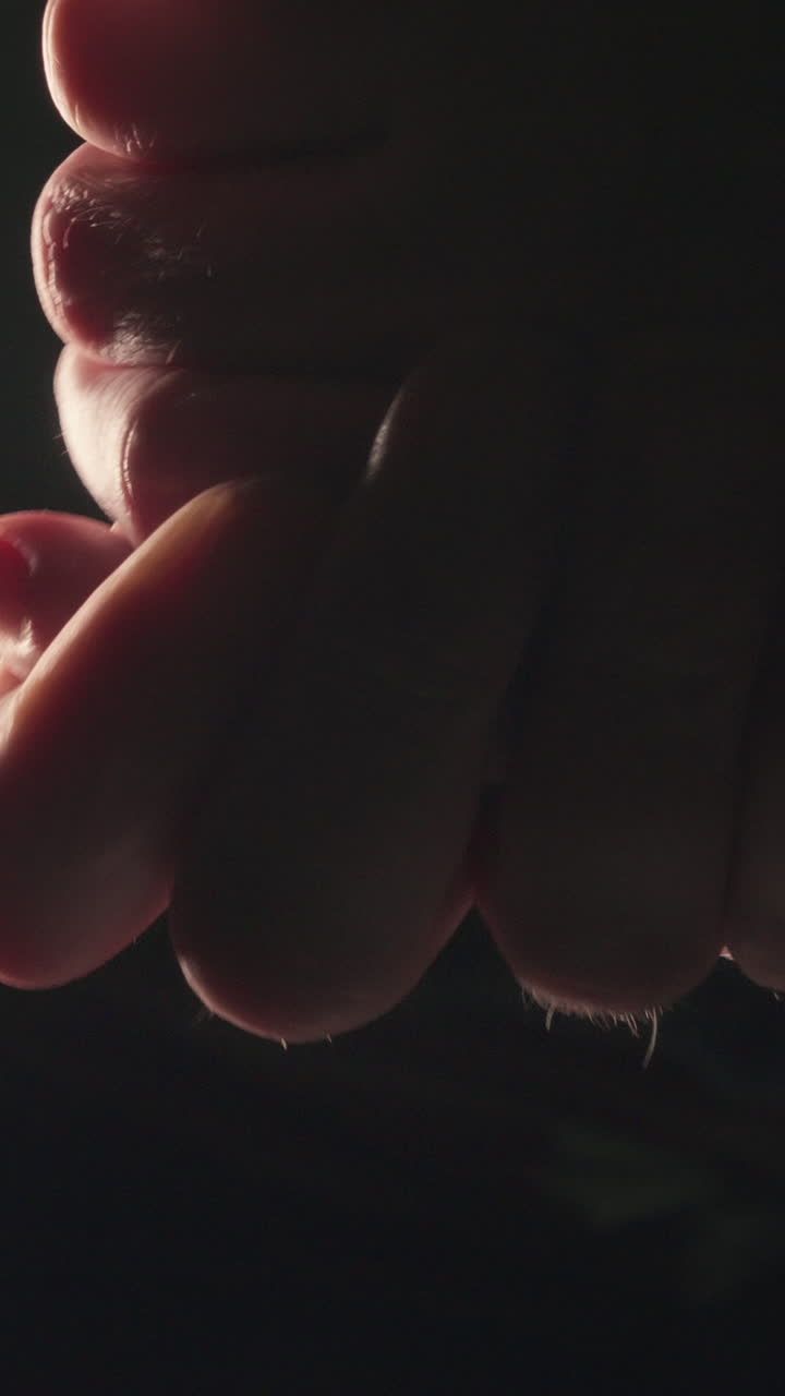 Primo piano verticale estremo di una persona che si strofina i palmi e le dita in condizioni di scarsa illuminazione. Ideale per temi di tensione, attesa, freddo e stati d'animo.