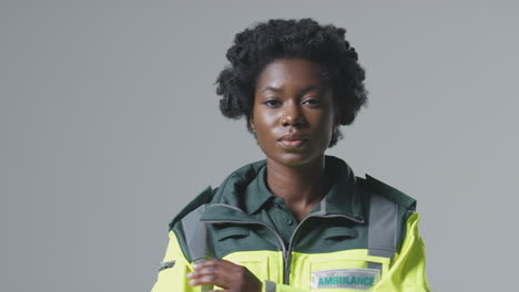 studio portrait of serious young female paramedic in uniform against plain background