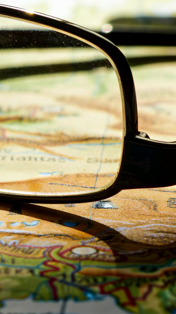 Vertical video: Framing eyeglass lens on desk map, camera capturing route details, light shifting