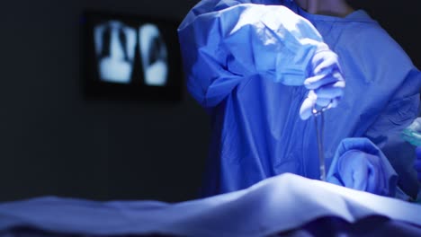 mid section of surgeon wearing protective clothing holding scissors in operating theatre