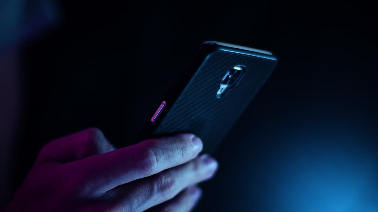 Thumb scrolling on a smartphone close up in a dark room with purple and blue lighting