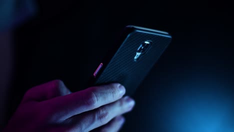 thumb scrolling on a smartphone close up in a dark room with purple and blue lighting