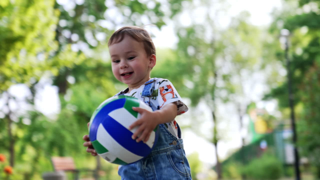 Adorable little kid carries his ball. Cute smiling baby runs up to camera. Close up.