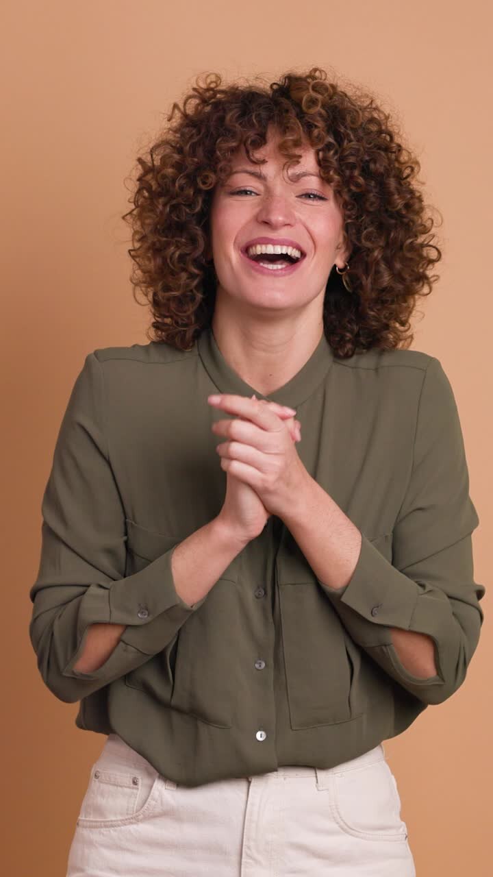 Giovane donna entusiasta che batte le mani e sorride su sfondo beige. Orientamento verticale