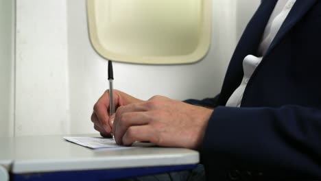 close up of a man writing on an immigration form paper on an airliner plane