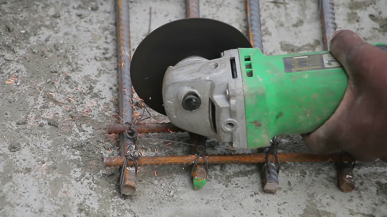 Indian mason worker cutting steel bars for reinforcement mesh construction with sparks flying from a grinder