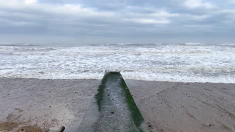 concrete groyne on hendon beach with rough north sea waves crashing onto the sand