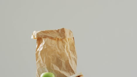 sándwich de mantequilla de maní y jalea con manzana y bolsa de papel contra un fondo blanco