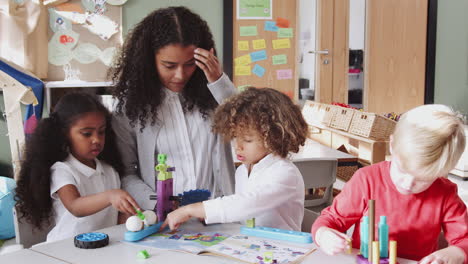 female infant school teacher helping children using construction toys in classroom