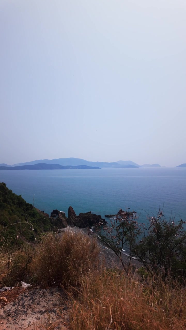 Orang-orang menikmati pemandangan dari Diem Ngam Bien di Na Trang, Vietnam. Mereka mengambil foto air dan pulau-pulau. Cuaca cerah dan terang di siang hari.