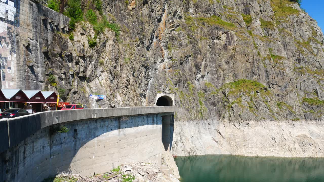 Panoramic views of a scenic mountain lake, dam, and road with tourists