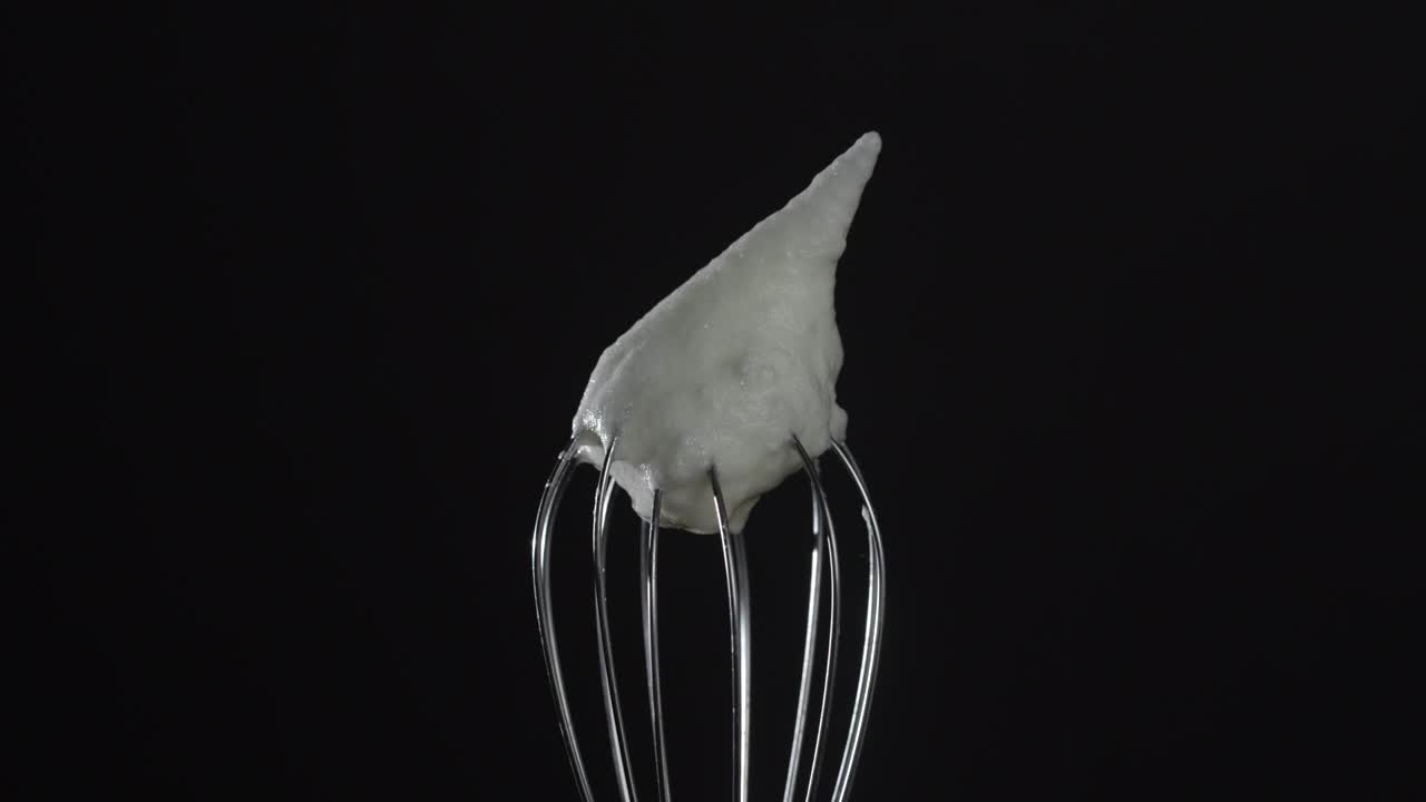 Metal whisk with whipped egg whites, isolated on black background