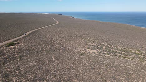 Drone-aerial-of-a-van-driving-on-a-country-road-by-a-beautiful-ocean