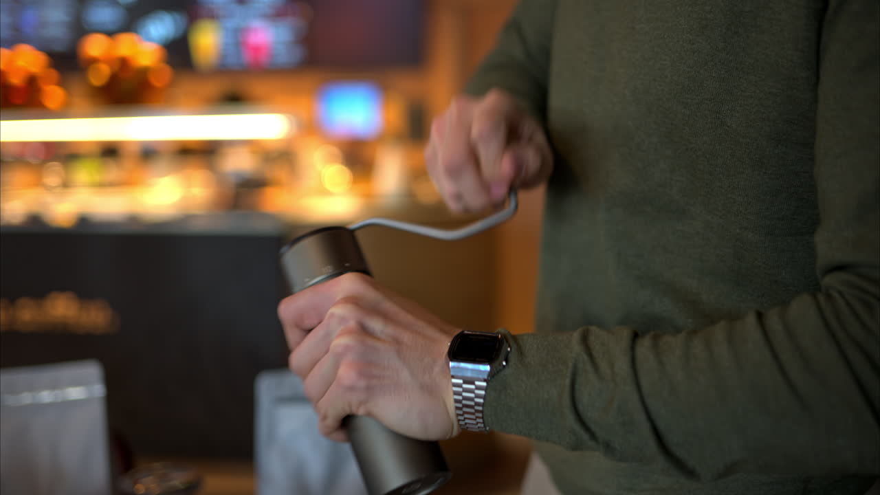 Close up of a man using a manual coffee grinder in a cafe