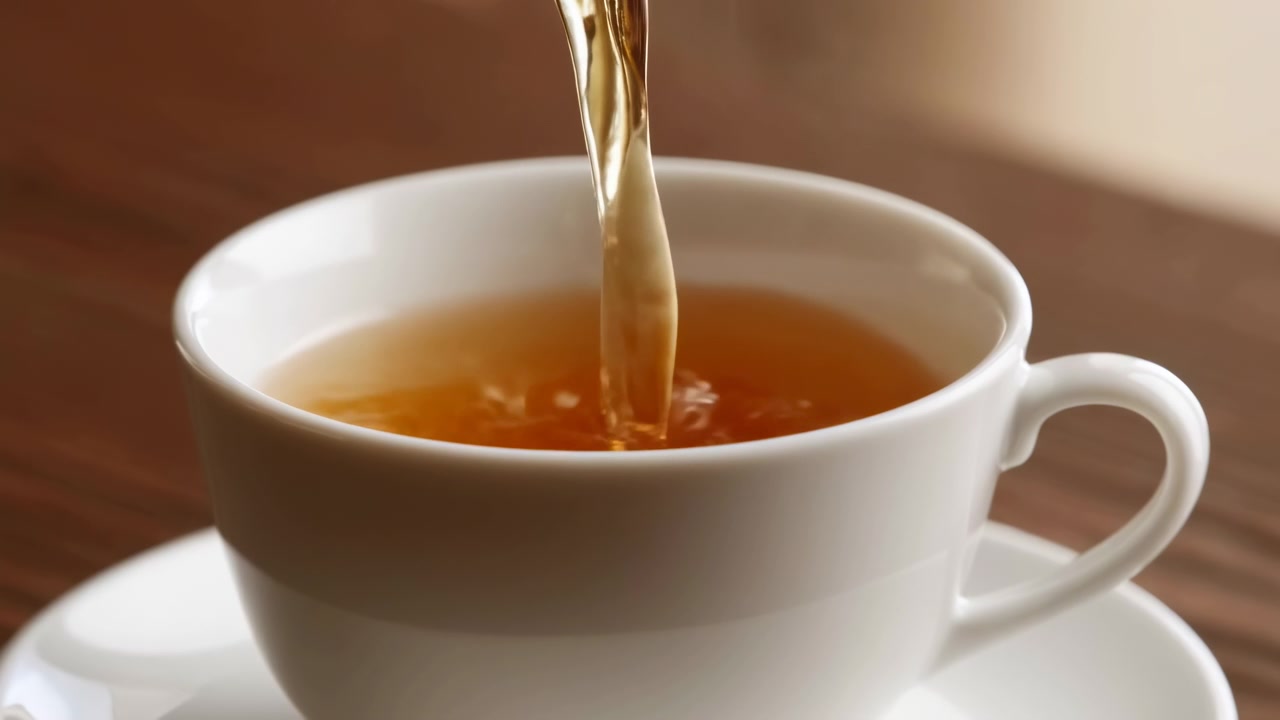 Primo piano che mostra tè dorato versato in una tazza bianca, con increspature superficiali e livello del liquido in aumento visibili dall'inizio alla fine su un tavolo di legno sotto un'illuminazione calda e soffusa