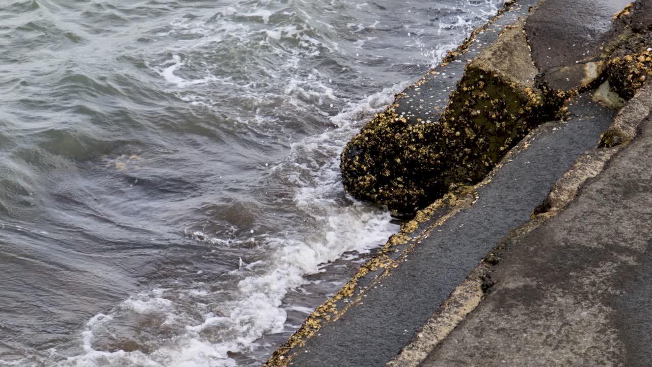 A close-up handheld shot of waves crashing against the stairs of a pier on a lake in Auckland, New Zealand