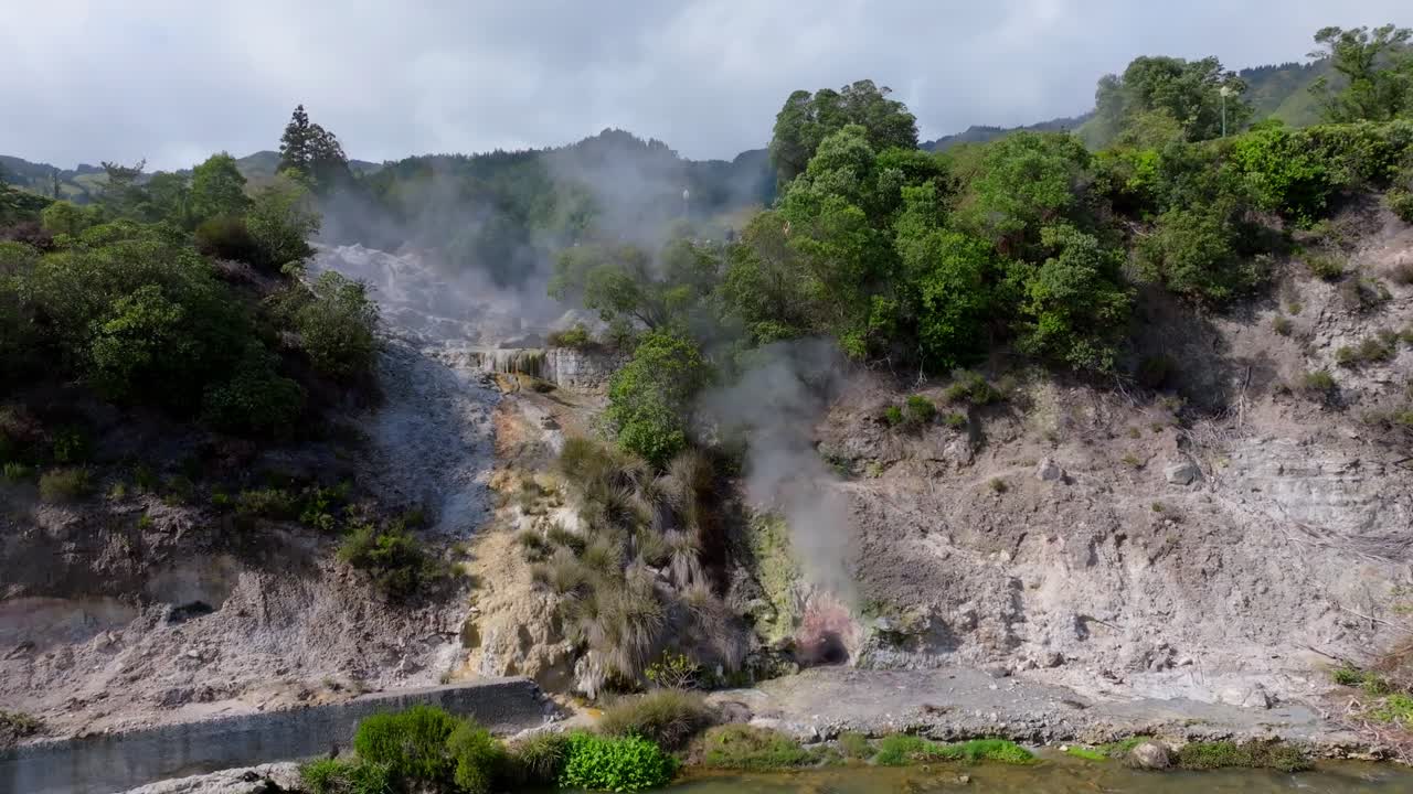 Pemandangan udara fumarol Furnas tempat uap naik dari lubang panas bumi, dikelilingi oleh bebatuan gelap dan tekstur vulkanik yang kontras di Azores, Portugal.