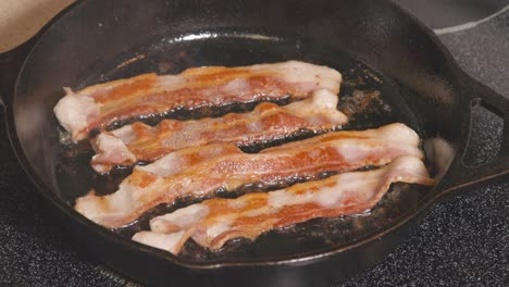 sartén de hierro fundido en la estufa girando tocino dorado