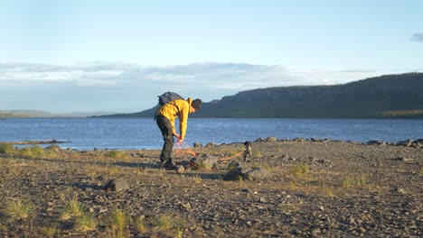 camper man tying his little dog in the campsite around rock near lake - push in wide slow-motion shot