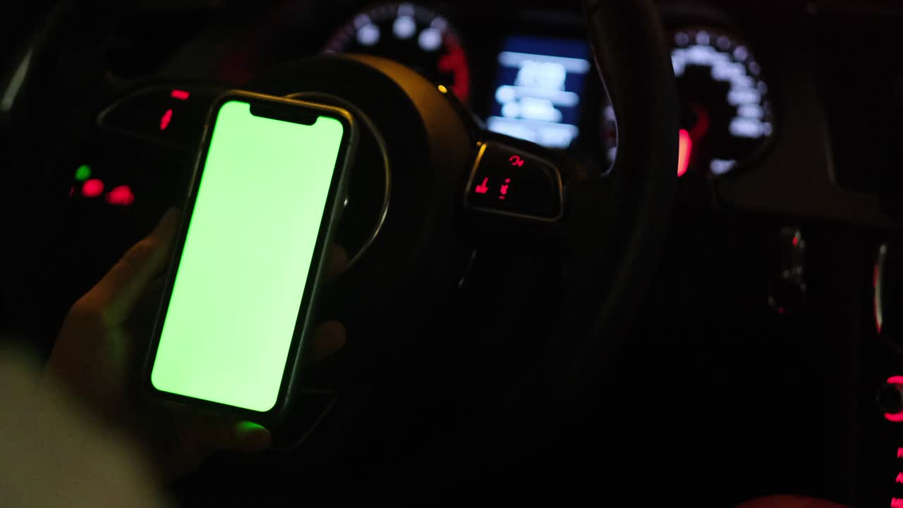 Driver's hand using green screen phone in car at night