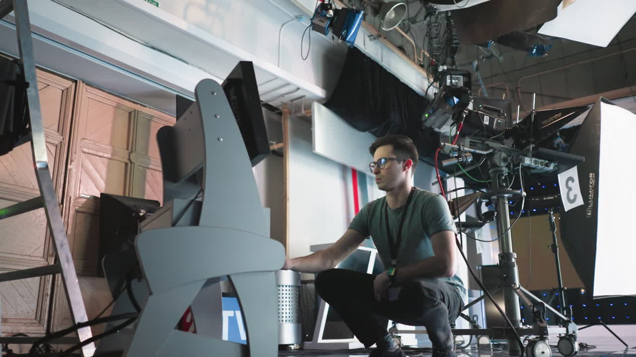 Man crouching in professional studio, adjusting digital monitor and timer settings on equipment, focused on work in high-tech filming environment, production process in progress