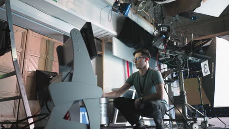 man crouching in professional studio, adjusting digital monitor and timer settings on equipment, focused on work in high-tech filming environment, production process in progress