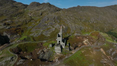copper mine, allihies, county cork, ireland, september 2024. drone pulls backwards and ascends from a close up of the ruined structure on a rocky mountain slope lit by bright sunshine.