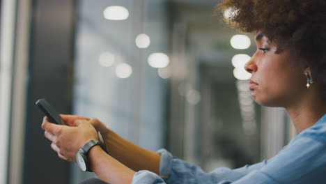 Stressed-Young-Businesswoman-Sitting-On-Floor-In-Corridor-Of-Modern-Office-With-Phone