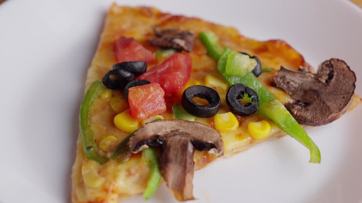 Primo piano di una mano che mette un'oliva su una pizza vegetariana con funghi e paprika