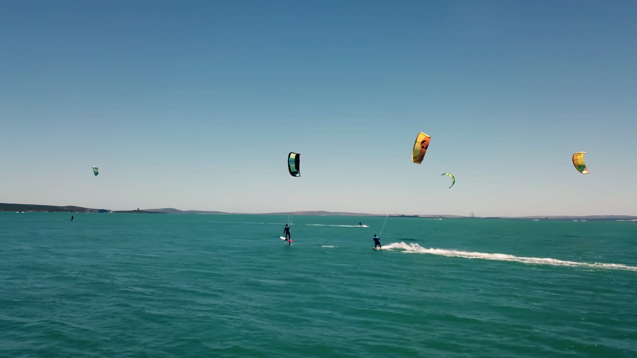 남아프리카 케이프 타운의 탁 트인 바다에서 푸른 하늘과 청록색 물을 배경으로 아름다운 자연광 속에서 무인 항공기에 의해 쫓기는 전문 수상 스포츠 카이트 서퍼