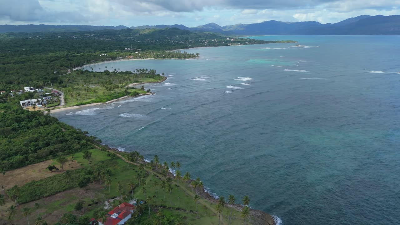 Aerial backwards shot of coastline with Caribbean seas during cloudy day. Green island along Samana, Dominican Republic.