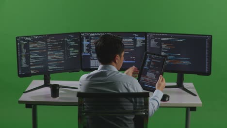 back view of asian man developer working with tablet while write code with multiple computer screens in green screen studio