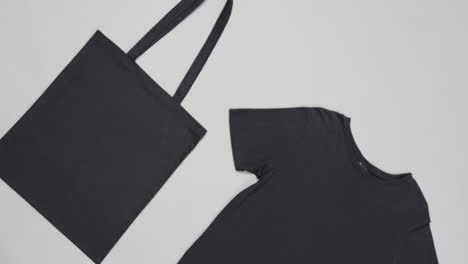 primer plano de una bolsa negra y una camiseta sobre un fondo blanco, con espacio de copia, cámara lenta