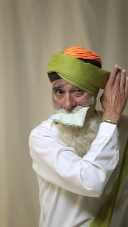 una toma de video vertical de un anciano sikh con barba atando tela para un turbante contra un fondo plano