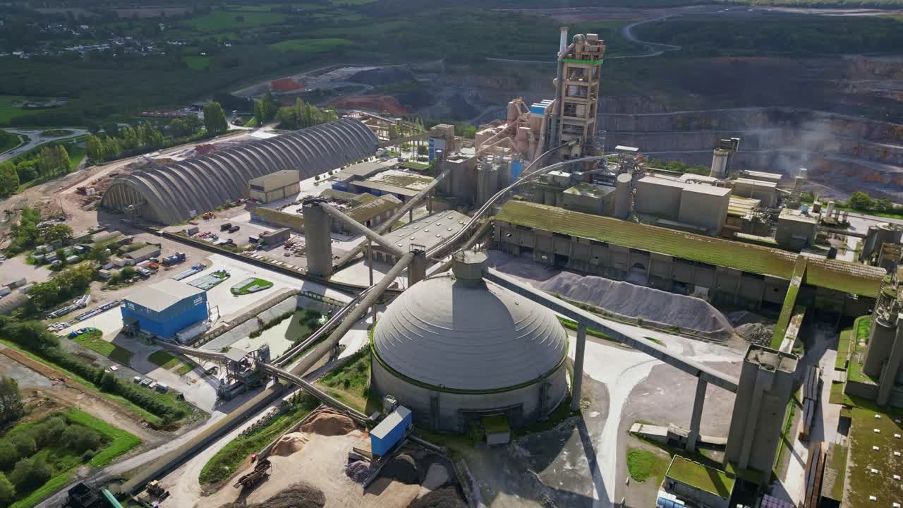 Flyover aerial of industrial quarry showing full cement facility and logistics area in rural Mayenne France