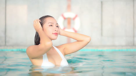 hot attractive asian woman pushing back wet hair in swimming pool - bust shot