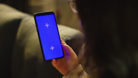 close up over the shoulder shot of woman spending evening at home sitting on sofa looking at blue screen mobile phone 1