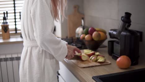 Woman-at-kitchen-cutting-apple-with-a-knife-on-a-wooden-cutting-board-to-make-juice